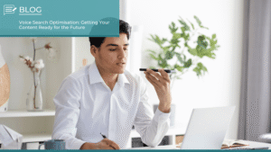 Man in a white shirt using voice command on a smartphone while working at a desk, symbolising voice search optimisation for digital content.