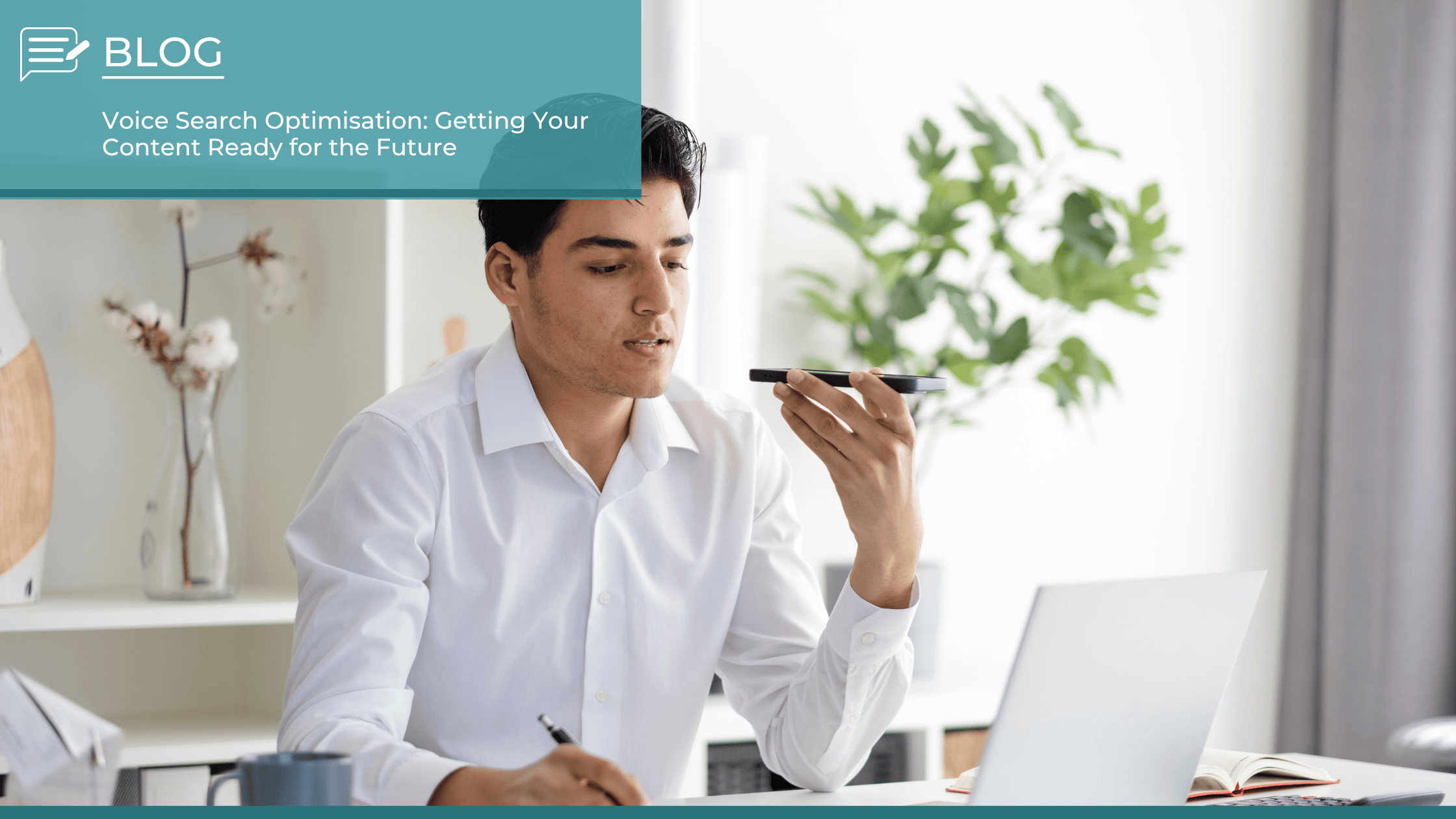 Man in a white shirt using voice command on a smartphone while working at a desk, symbolising voice search optimisation for digital content.